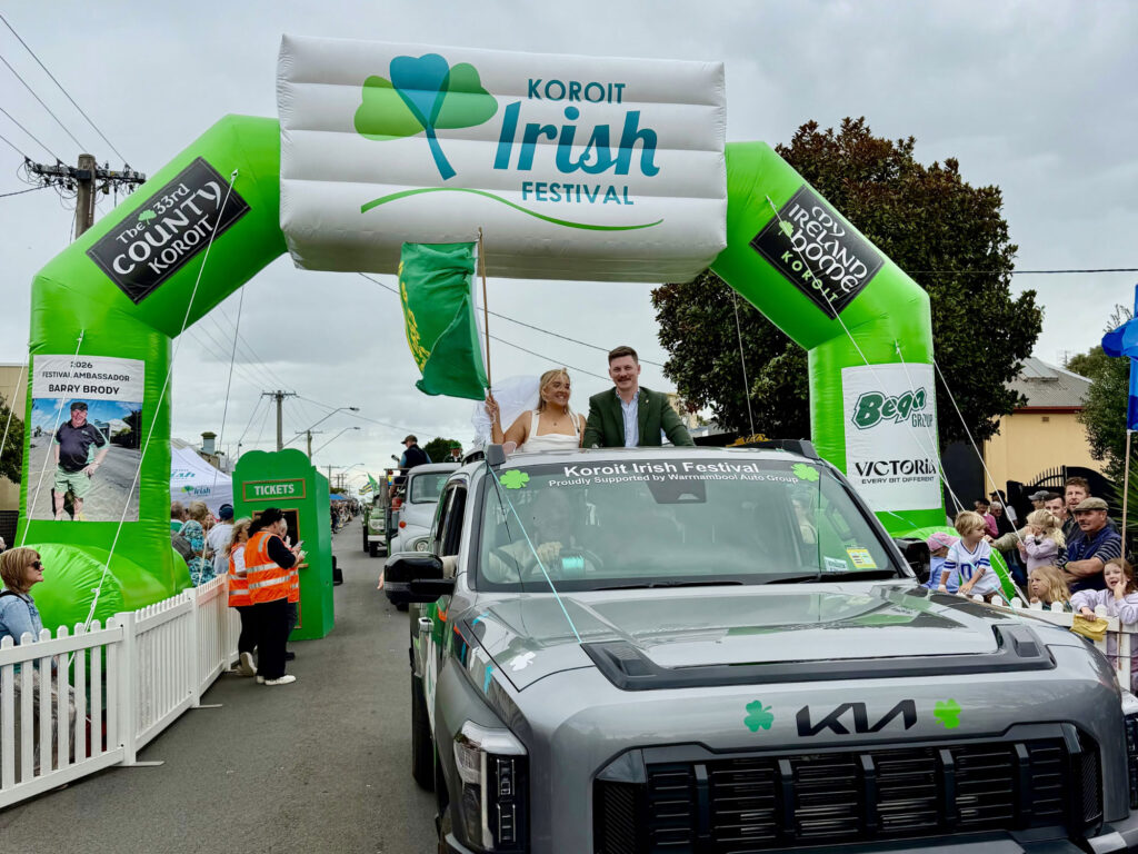 A large green custom inflatable arch with a white 3D header and interchangeable sponsor banners stands over a parade route in Koroit, Victoria.